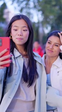 İki mutlu çok ırklı kadın dışarıda dolaşırken arkadaşlarıyla görüntülü konuşma yapmak için akıllı telefon kullanıyor.