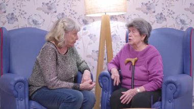 Huzurevindeki koltuklarda oturup rahatça sohbet eden iki yaşlı kadın arkadaş.