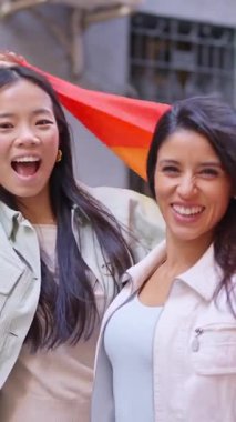 Gökkuşağı bayrağını sallayan ve bir geçit töreninde birlikte gülümseyen çok ırklı genç bir kadın.