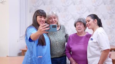 Yaşlı kadınlar ve bir hemşire asistanı huzurevinde selfie çekiyorlar.