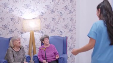 Mutlu torun, huzurevinde oturan büyükannesini kucaklıyor ve öpüyor.