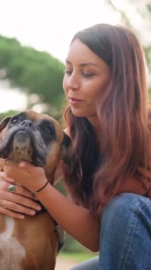 Parkta sevgili boksör köpeğine sevgi gösteren genç bir kadın.