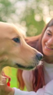 Güzel genç bir kadın gülümsüyor ve parkta köpeğini okşuyor.