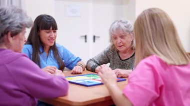 Yaşlı kadın ve hemşireler bilişsel terapi için bakımevinde masa oyunu oynuyorlar.