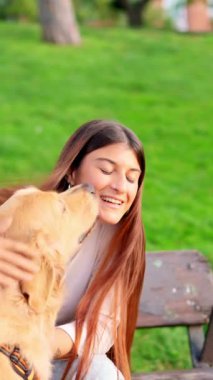 Güzel yeşil bir parkta sevgili köpeğinden öpücük ve kucak alan mutlu genç bir kadın.