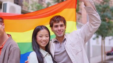 LGBTQ artı gururu temsil eden gökkuşağı bayrağı tutan mutlu genç adam ve kadın.