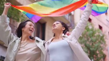 Gökkuşağı bayrağını sallayan neşeli lezbiyen çift sokakta gururu kutluyor.