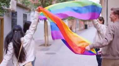 Eşcinsel onur yürüyüşü sırasında ellerinde gökkuşağı bayrağı tutan bir grup mutlu çok ırklı arkadaş.
