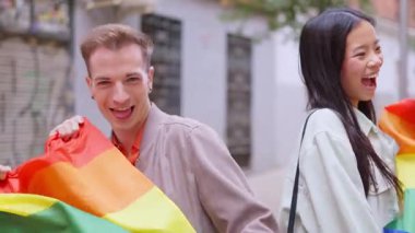 Mutlu çok ırklı arkadaşlar gülümseyerek ve ellerinde gökkuşağı bayrağı tutarak eşcinsel onur yürüyüşü yapıyorlar.