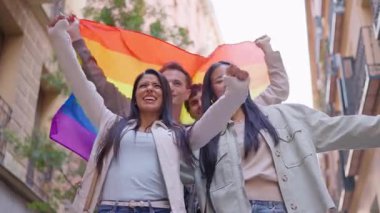 Eşcinsel onur yürüyüşü sırasında ellerinde gökkuşağı bayrağı tutan bir grup mutlu çok ırklı arkadaş.