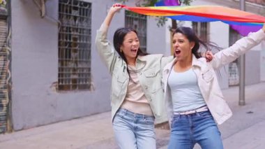 İki mutlu çok ırklı kadın bir geçit töreninde lgbtq artı bayrağıyla gülüyor ve yürüyorlar.