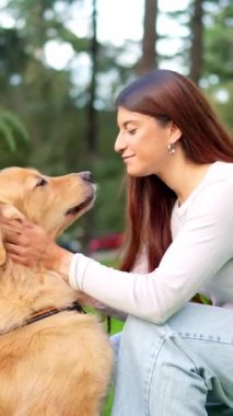 Parkta yüzünü yalarken Golden Retriever köpeğini okşayan bir kadın.