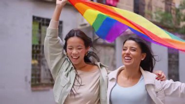 Gurur yürüyüşü sırasında gökkuşağı bayrağı sallayan çok ırklı genç lezbiyen çift