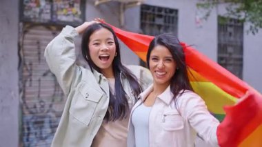 Gökkuşağı bayrağını sallayan ve bir geçit töreninde birlikte gülümseyen çok ırklı genç bir kadın.