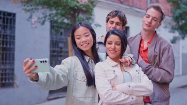 Mutlu çok ırklı arkadaş grubu akıllı telefonuyla selfie çekiyor ve şehirde eğleniyor.