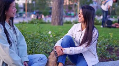 Parkta oturmuş güneşli bir günün tadını çıkarırken gülümseyen iki farklı genç kadın.