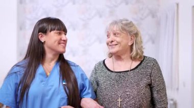 Yaşlı bir kadını destekleyen neşeli hemşire, ilgi, yardım ve dostça bir ilişki gösteriyor.