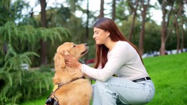 Parkta yüzünü yalarken Golden Retriever köpeğini okşayan bir kadın.