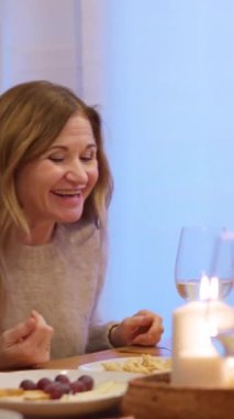 Neşeli bir kadın mum ışığında şarap ve aperatiflerle canlı bir akşam yemeğinde sohbet ediyor.