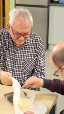 Fiziksel engelli bir adama mutfakta tabakta yemek servis etmesi için yardım eden bir adam.