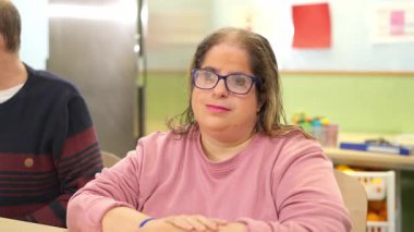 Fiziksel engelli, kendine güveni tam bir kadın. Gözlük takıyor, kameraya bakıyor ve nazikçe gülümsüyor.