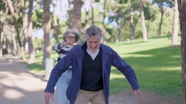 Neşeli gri saçlı yaşlı çift eğlenirken koca karısını sırtında taşıyor.