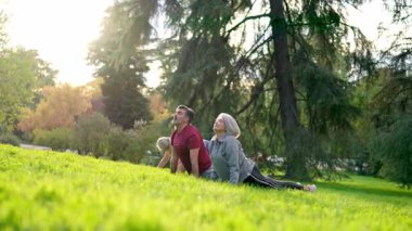 Olgun erkek ve kadın yeşil çimenler üzerinde yoga kursu sırasında kobra pozu veriyorlar.