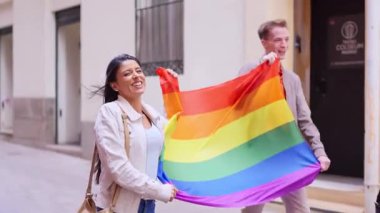 Mutlu çift gurur ayını gökkuşağı bayrağıyla kutluyor ve şehirde gülümsüyor.