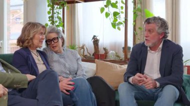 Bir grup olgun ve kıdemli arkadaş bir kanepede otururken konuşuyor ve gülüyorlar.