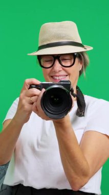 Yeşil ekran arka planı olan bir stüdyoda dijital kamera kullanan neşeli yaşlı turist.
