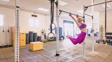 Barfiks çubuğunda asılı bir kadın, modern bir spor salonunda egzersiz yapıyor.