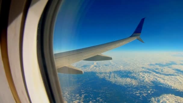 Flugzeug fliegt am blauen Himmel durch die weißen Wolken. Blick auf den Flugzeugflügel aus dem Fenster. — Stockvideo