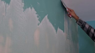 Duvarı spatulayla hizalayan adam macun ve spatula duvarıyla çalışıyor.