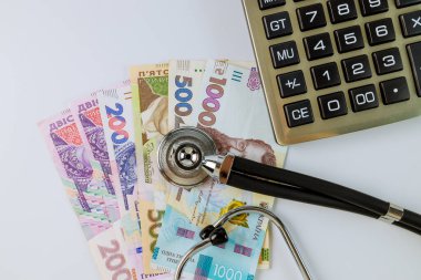 Finansal hesaplamalar, Ukrayna 'da beyaz arka planda banknotları olan bir para aralığındaki fonendoskop steteskobu ile yapılan tıbbi tedavi ödeme hesapları.