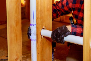 İnşaat halindeki bir tesisatçı, yeni plastik drenaj üzerine beyaz bir PVC boru yapıştırıyor.