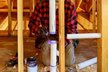 Tesisatçı, çalışma alanındaki PVC drenaj borusuna yapıştırıcı sürüyor..