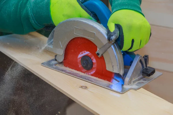 Carpenter using hand circular saw for cutting wooden boards with power tools at woodworking sawmill.