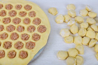 Yuvarlak bir tahtanın üzerinde geleneksel bir Slav ulusal yemeği, un ve etten hamur köftesi pişirme sürecinin üst görünümü