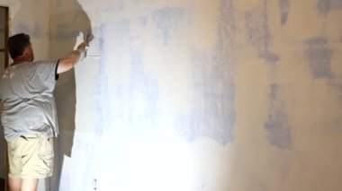 Adamın biri duvardaki beyaz alçıya bir spatula yapıştırıyor..