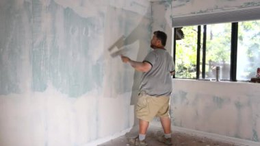 İnşaat işçisi alçıdan alçıya alçıpan duvarda son rötuşları yapıyor.