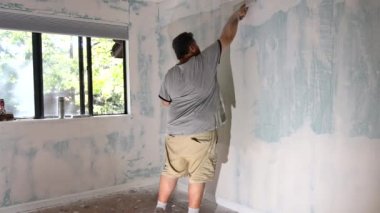 İnşaatçı duvara sıva yapıştırır. Duvarı tamir eden bir spatula tutar. Bir macun bitirir.