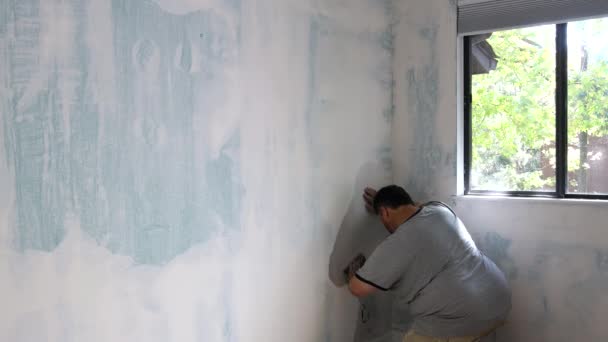Stukadoor gladstrijkt de muren met schuurpapier mannelijke hand van een werknemer. — Stockvideo