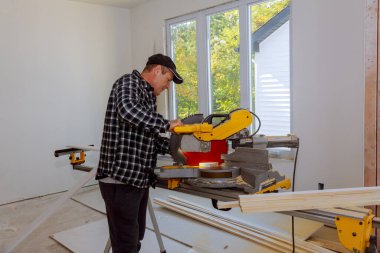 İnşaatçı ahşap süpürgelik ekipmanlarını kesmek için dairesel testere kullanıyor.