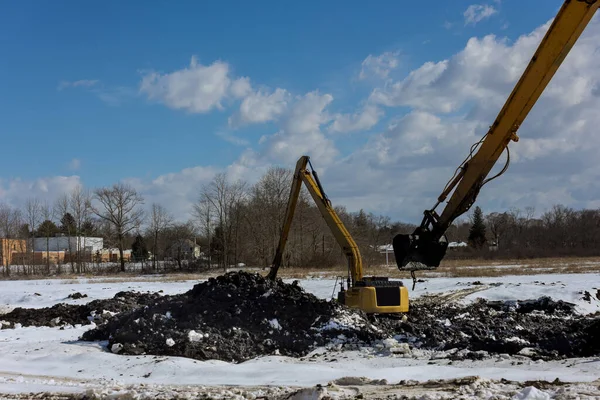 冬のバックホー掘りのピットで地球移動に取り組んで掘削機の建設現場での掘削中の重機 — ストック写真