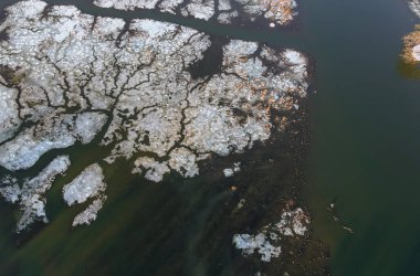 Güneşli bir günde, nehir kıyısında, parlak bahar güneşinin altında eriyen buz parçaları.
