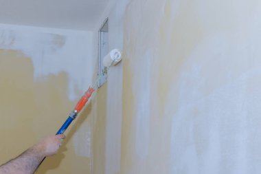 Ressamın arka görünüşü odada bir silindirle duvarı boyuyor.