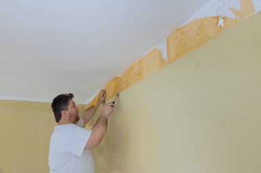 Duvar odasını yenileme işlemi eski duvar kağıdını duvardan söküp bir spatulayla ev onarımına hazırlanma süreci.