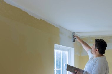 Profesyonel inşaat işçisi, oda tadilatı sırasında duvarlara alçı kaplama uyguluyor.