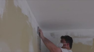 İşçi, evi yenileme sırasında kum malası kullanarak alçıpan çamurunu zımparalıyor.