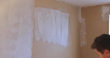 Ressamın arka görünüşü duvarı silindirle boyuyor.